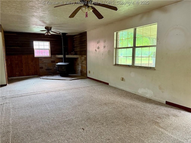 3112 Cicerone Rd, Charleston, WV 25320 - unfurnished living room featuring a textured ceiling, ceiling fan, a wood stove, carpet floors, and wooden walls