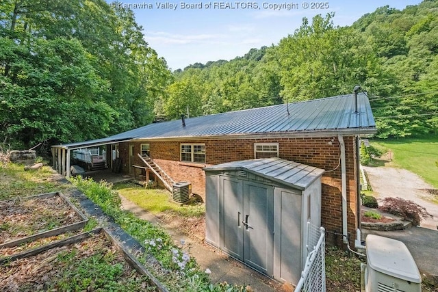 169 Burning Springs Dr, Belle, WV 25015 - back of house featuring metal roof, a vegetable garden, brick siding, a wooded view, and central air condition unit