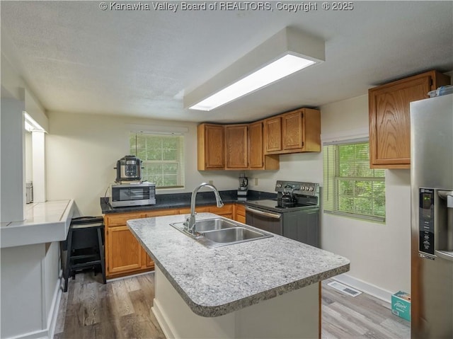 3742 Greenview Rd, South Charleston, WV 25309 - kitchen featuring appliances with stainless steel finishes, light wood finished floors, an island with sink, and brown cabinets