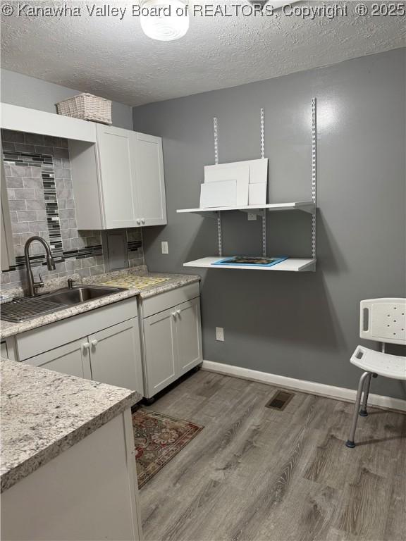 194 Shawnee Ests, Winfield, WV 25213 - kitchen with wood finished floors, a textured ceiling, decorative backsplash, white cabinetry, and light stone counters