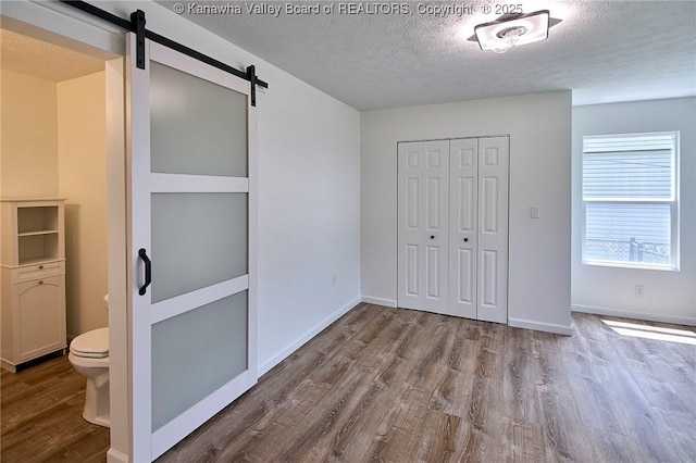 911 Dupont Ave, Nitro, WV 25143 - unfurnished bedroom featuring a barn door, wood finished floors, a textured ceiling, and a closet