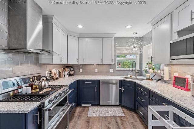 916 Amherst Dr, Charleston, WV 25302 - kitchen with appliances with stainless steel finishes, wall chimney exhaust hood, blue cabinets, light wood-style floors, and recessed lighting