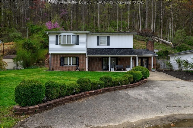 969 Airport Rd, Chapmanville, WV 25508 - traditional-style house featuring brick siding, a front yard, concrete driveway, covered porch, and a wooded view