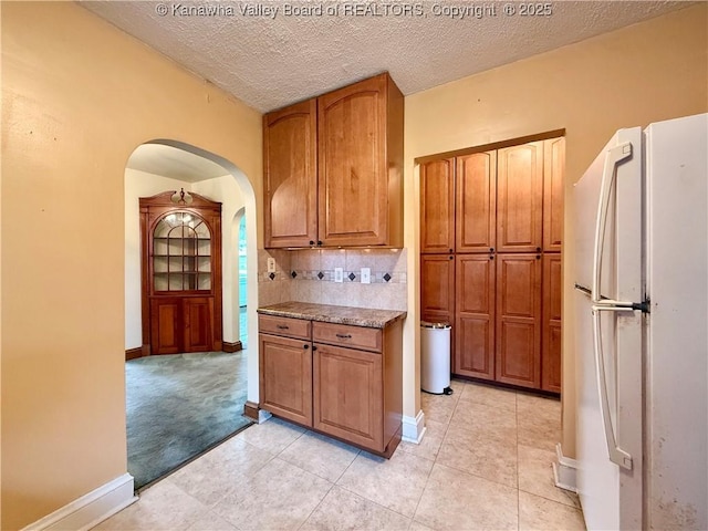 108 W Main St, Belle, WV 25015 - kitchen featuring freestanding refrigerator, arched walkways, backsplash, brown cabinets, and a textured ceiling
