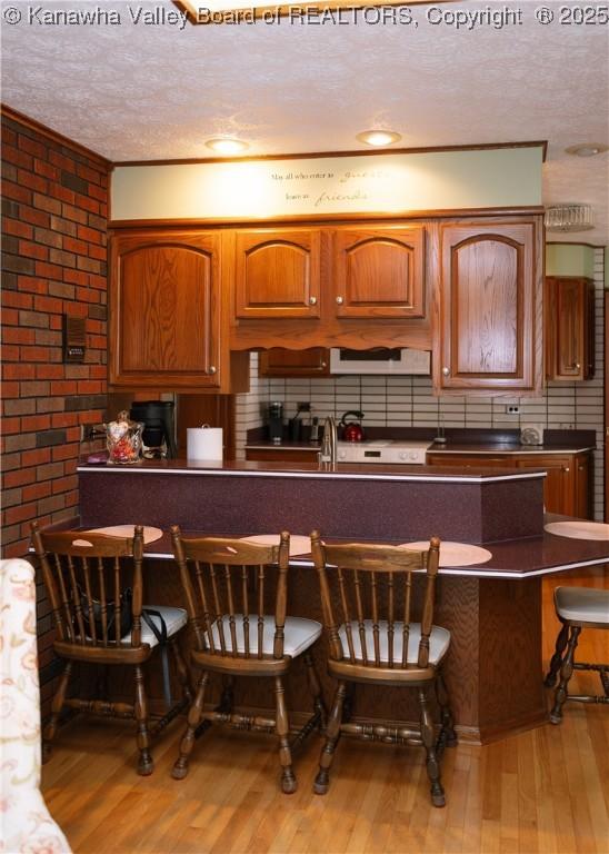 35 Belpac Cir, Logan, WV 25601 - kitchen with a textured ceiling, light wood-style flooring, a kitchen bar, dark countertops, and decorative backsplash