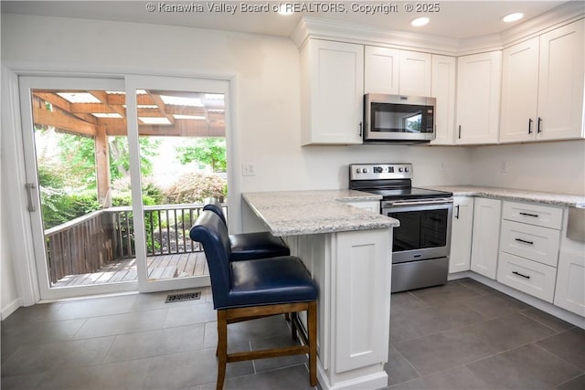 1516 Fenton Cir, Nitro, WV 25143 - kitchen with stainless steel appliances, white cabinets, a breakfast bar, dark tile patterned flooring, and recessed lighting