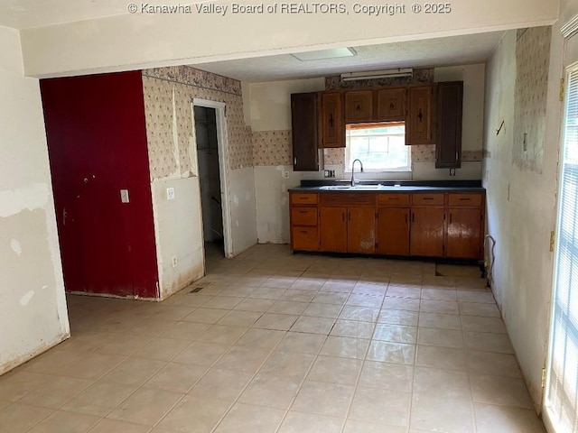 134 Ferguson Ct, Huntington, WV 25701 - kitchen with wallpapered walls, light tile patterned floors, brown cabinetry, wainscoting, and dark countertops