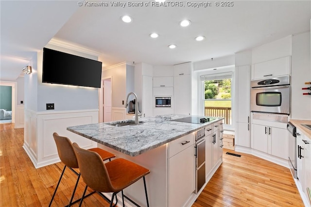 815 Chappell Rd, Charleston, WV 25304 - kitchen featuring stainless steel appliances, white cabinetry, a center island with sink, wainscoting, and light wood-style flooring
