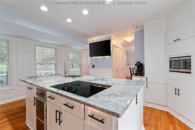815 Chappell Rd, Charleston, WV 25304 - kitchen featuring stainless steel microwave, black electric cooktop, a center island with sink, a decorative wall, and light wood-style floors