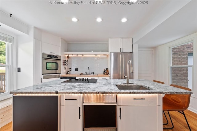 815 Chappell Rd, Charleston, WV 25304 - kitchen featuring stainless steel appliances, light wood finished floors, white cabinetry, a kitchen island with sink, and light stone counters