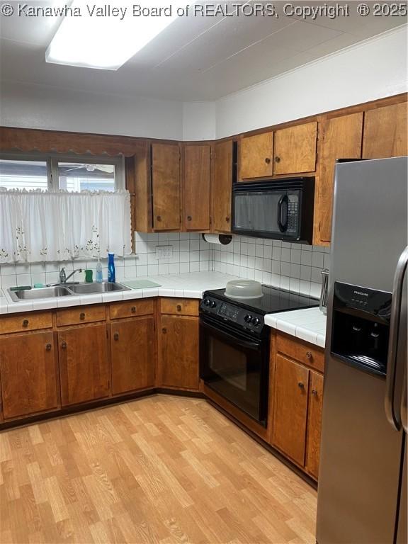 510 S Railway St, Cedar Grove, WV 25039 - kitchen with black appliances, light wood-type flooring, tasteful backsplash, tile counters, and brown cabinetry