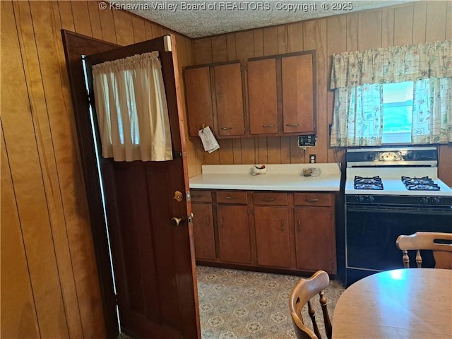 588 Saunders Creek Rd, Milton, WV 25541 - kitchen with black range with gas cooktop, wooden walls, light countertops, brown cabinetry, and a textured ceiling