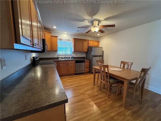 2314 Harrison Ave, Saint Albans, WV 25177 - kitchen with dark countertops, a ceiling fan, stainless steel appliances, brown cabinetry, and light wood-style flooring