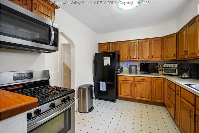 2526 Spring St, South Charleston, WV 25303 - kitchen featuring stainless steel appliances, light countertops, brown cabinetry, light flooring, and arched walkways