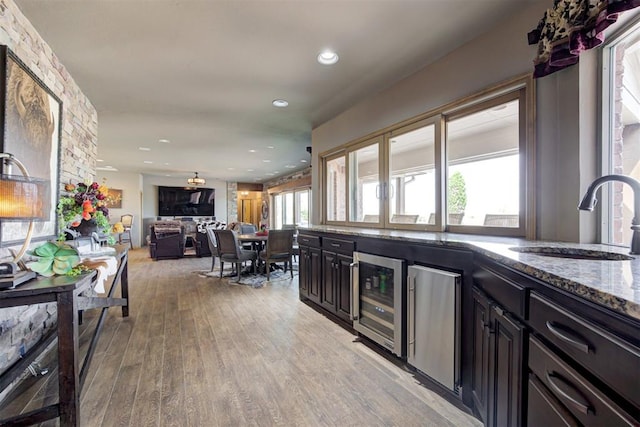 kitchen featuring wine cooler, sink, dark stone counters, and light wood-type flooring