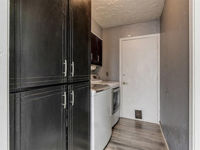 laundry area with cabinets, a textured ceiling, separate washer and dryer, and light hardwood / wood-style flooring