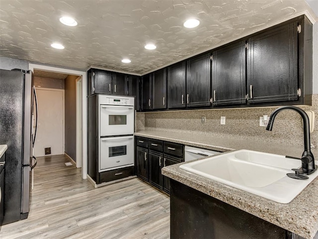 kitchen featuring stainless steel refrigerator, white double oven, sink, decorative backsplash, and light wood-type flooring