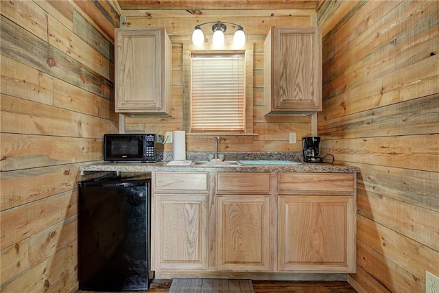 kitchen featuring wood walls, light brown cabinetry, black appliances, and sink