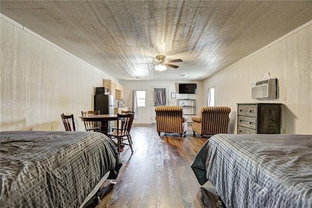 bedroom with ceiling fan, dark hardwood / wood-style flooring, an AC wall unit, and stainless steel refrigerator