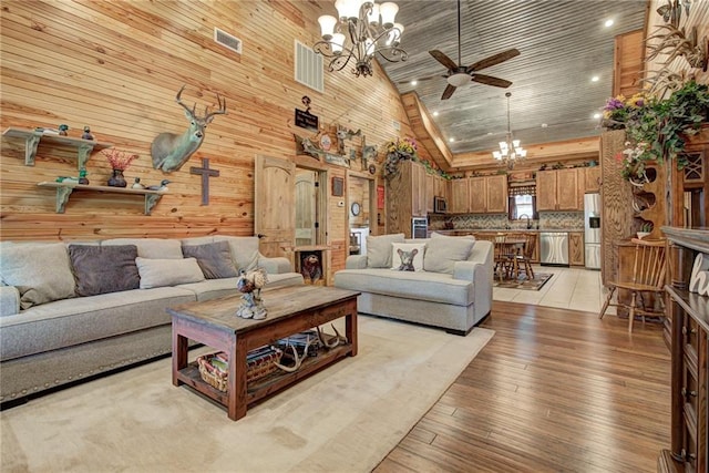 living room featuring ceiling fan with notable chandelier, light hardwood / wood-style floors, high vaulted ceiling, and wood walls