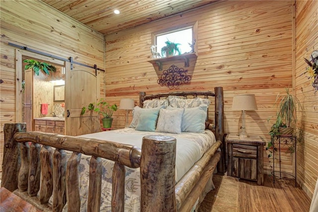 bedroom with wood ceiling, a barn door, hardwood / wood-style floors, connected bathroom, and wood walls