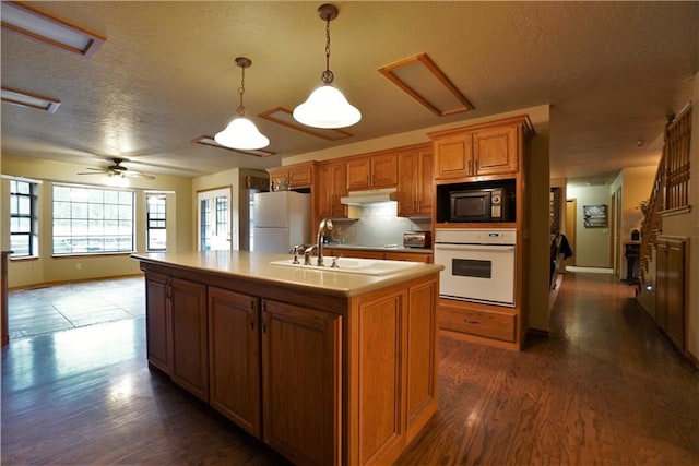 kitchen with white appliances, a kitchen island with sink, ceiling fan, decorative light fixtures, and dark hardwood / wood-style floors