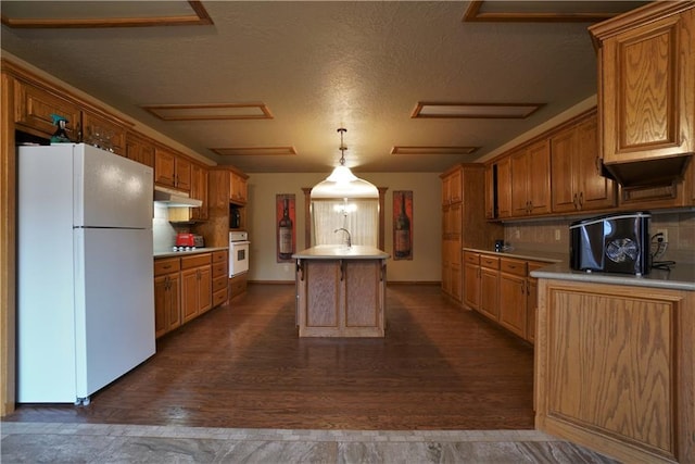 kitchen featuring white appliances, dark wood-type flooring, a textured ceiling, an island with sink, and tasteful backsplash