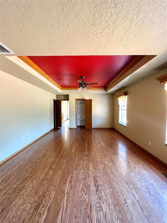 unfurnished living room featuring a textured ceiling, a tray ceiling, ceiling fan, crown molding, and hardwood / wood-style floors