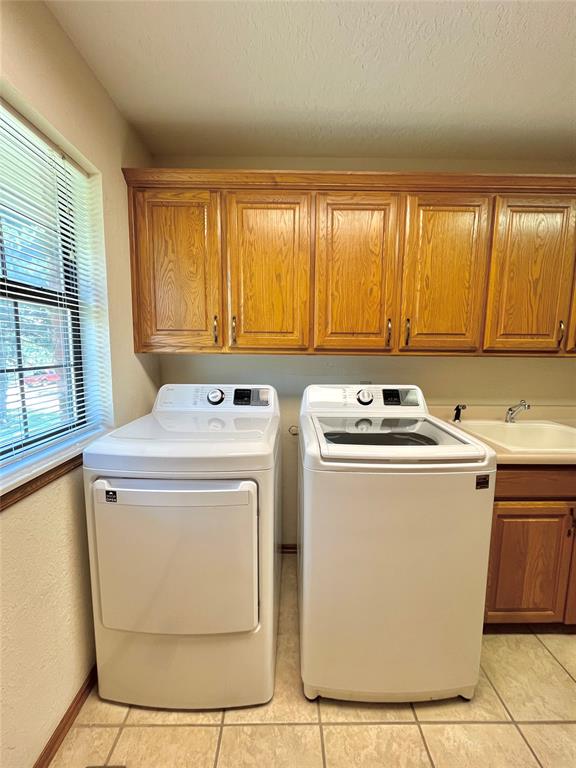 clothes washing area featuring cabinets, sink, washer and dryer, and light tile patterned flooring