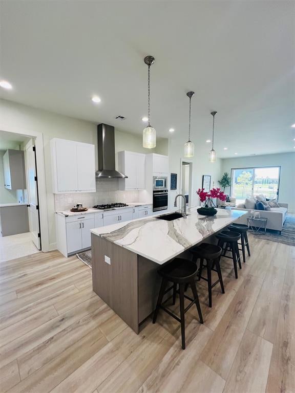 kitchen with stainless steel appliances, white cabinetry, a spacious island, and wall chimney range hood