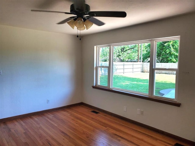 spare room featuring a ceiling fan, visible vents, wood finished floors, and baseboards