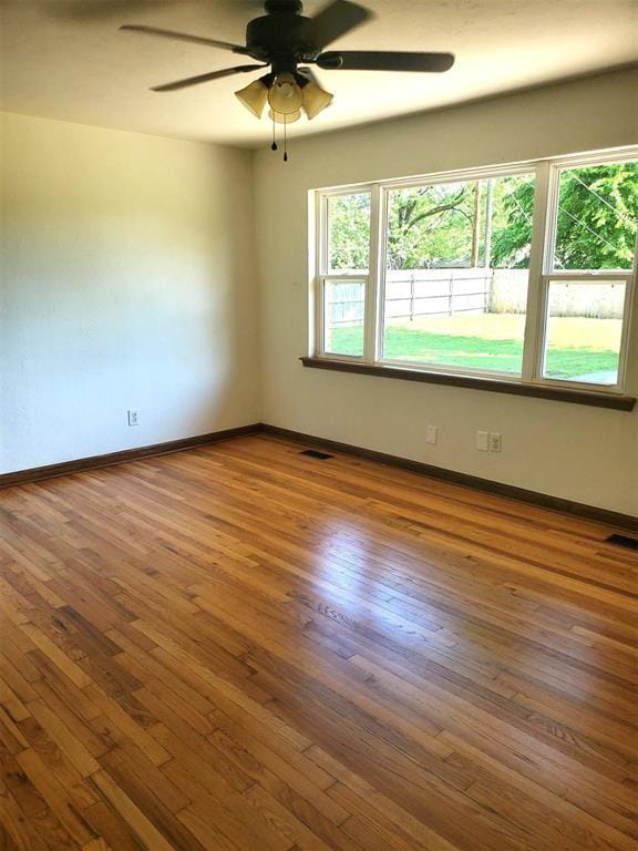 unfurnished room with wood-type flooring, a ceiling fan, plenty of natural light, and visible vents