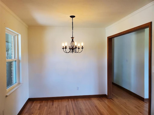 unfurnished room featuring a chandelier, wood finished floors, baseboards, and ornamental molding