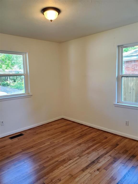 unfurnished room with a healthy amount of sunlight, visible vents, and wood finished floors