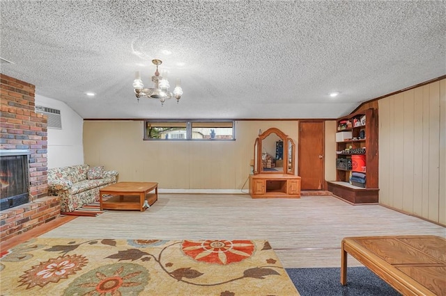 living room featuring a textured ceiling, wooden walls, an inviting chandelier, a fireplace, and lofted ceiling