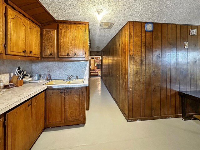 kitchen featuring a textured ceiling, backsplash, wooden walls, and sink