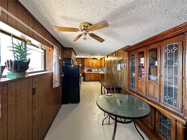 dining space with wooden walls, ceiling fan, and a textured ceiling