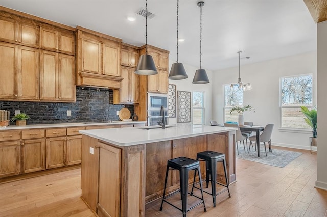 kitchen with stainless steel microwave, sink, decorative light fixtures, a center island with sink, and light wood-type flooring