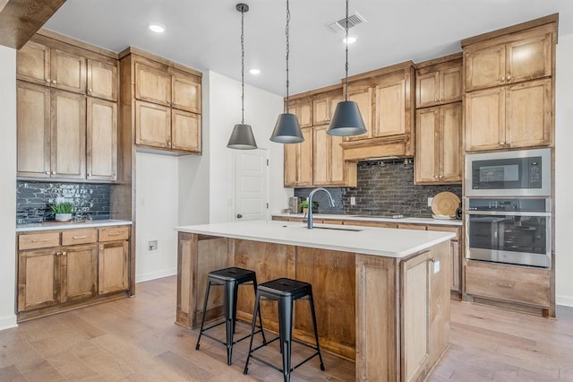 kitchen featuring sink, backsplash, a kitchen island with sink, appliances with stainless steel finishes, and light wood-type flooring