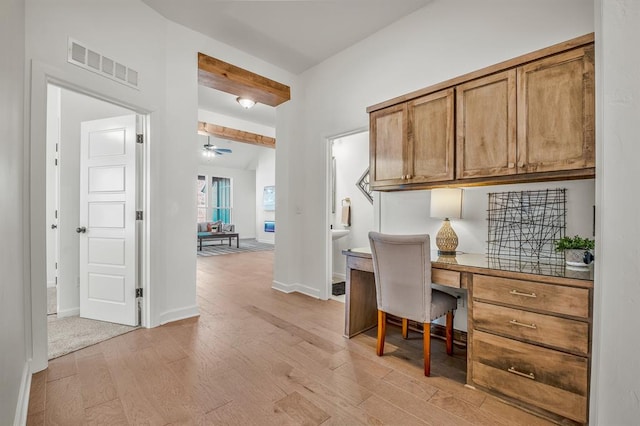 office space featuring beamed ceiling, built in desk, light hardwood / wood-style flooring, and ceiling fan