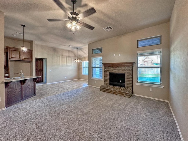 unfurnished living room featuring a textured ceiling, ceiling fan with notable chandelier, light carpet, and a brick fireplace