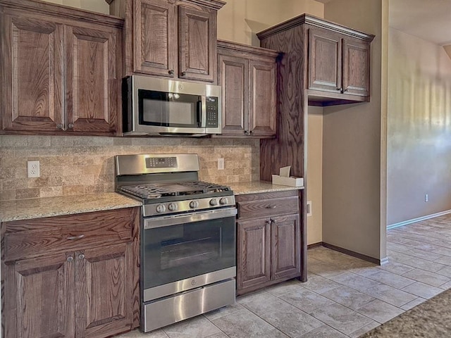 kitchen with backsplash, dark brown cabinetry, light stone counters, and appliances with stainless steel finishes