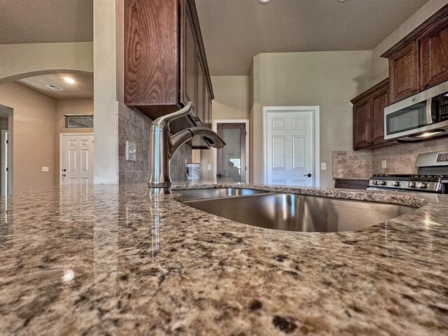 kitchen featuring backsplash, stone counters, sink, appliances with stainless steel finishes, and dark brown cabinets