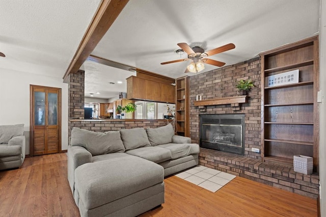 living room featuring light wood-type flooring, a fireplace, ceiling fan, built in features, and beamed ceiling