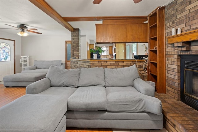 living room with beamed ceiling, wood-type flooring, a brick fireplace, and ceiling fan