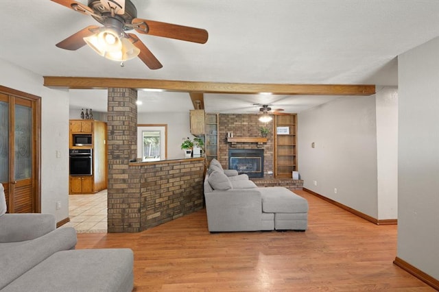 living room with beam ceiling, a brick fireplace, ceiling fan, and light wood-type flooring