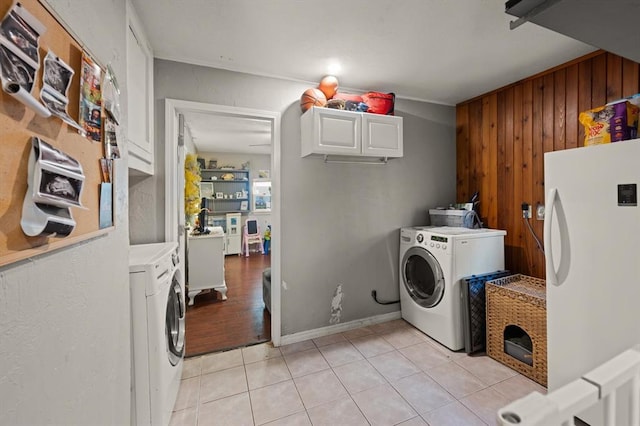 clothes washing area with wood walls, cabinets, light tile patterned floors, and separate washer and dryer