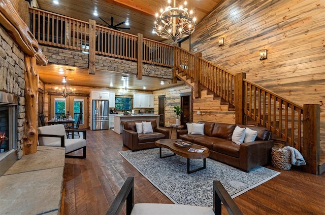 living room featuring a stone fireplace, a towering ceiling, dark hardwood / wood-style flooring, a chandelier, and wood ceiling