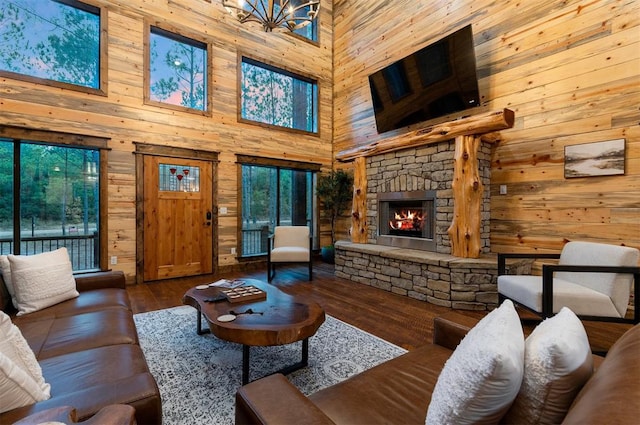 living room with a stone fireplace, dark wood-type flooring, wooden walls, and a towering ceiling