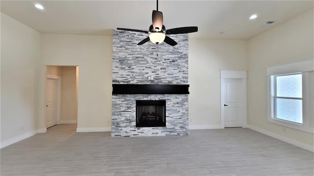 unfurnished living room featuring ceiling fan, a large fireplace, and light wood-type flooring